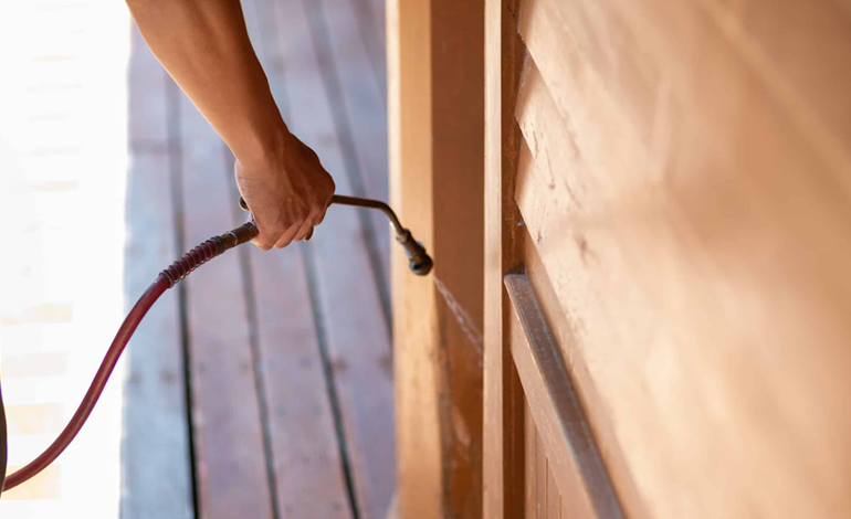 Applying pest control spray to wooden doors prevents infestations and moisture damage.